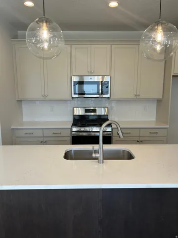 Kitchen island featuring a stainless steel sink, brushed nickel faucet, and light-toned countertop
