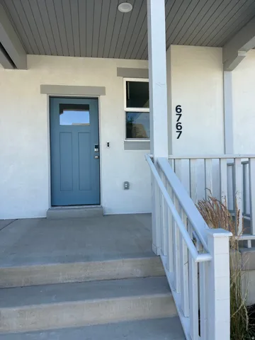 Modern stucco exterior featuring a blue paneled entry door with glass insert, a complementary white trim window, and concrete steps leading to the covered porch