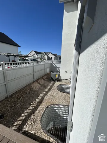 Gravel-lined side yard with a white picket fence, two window wells with grates, a visible AC unit, and a downspout