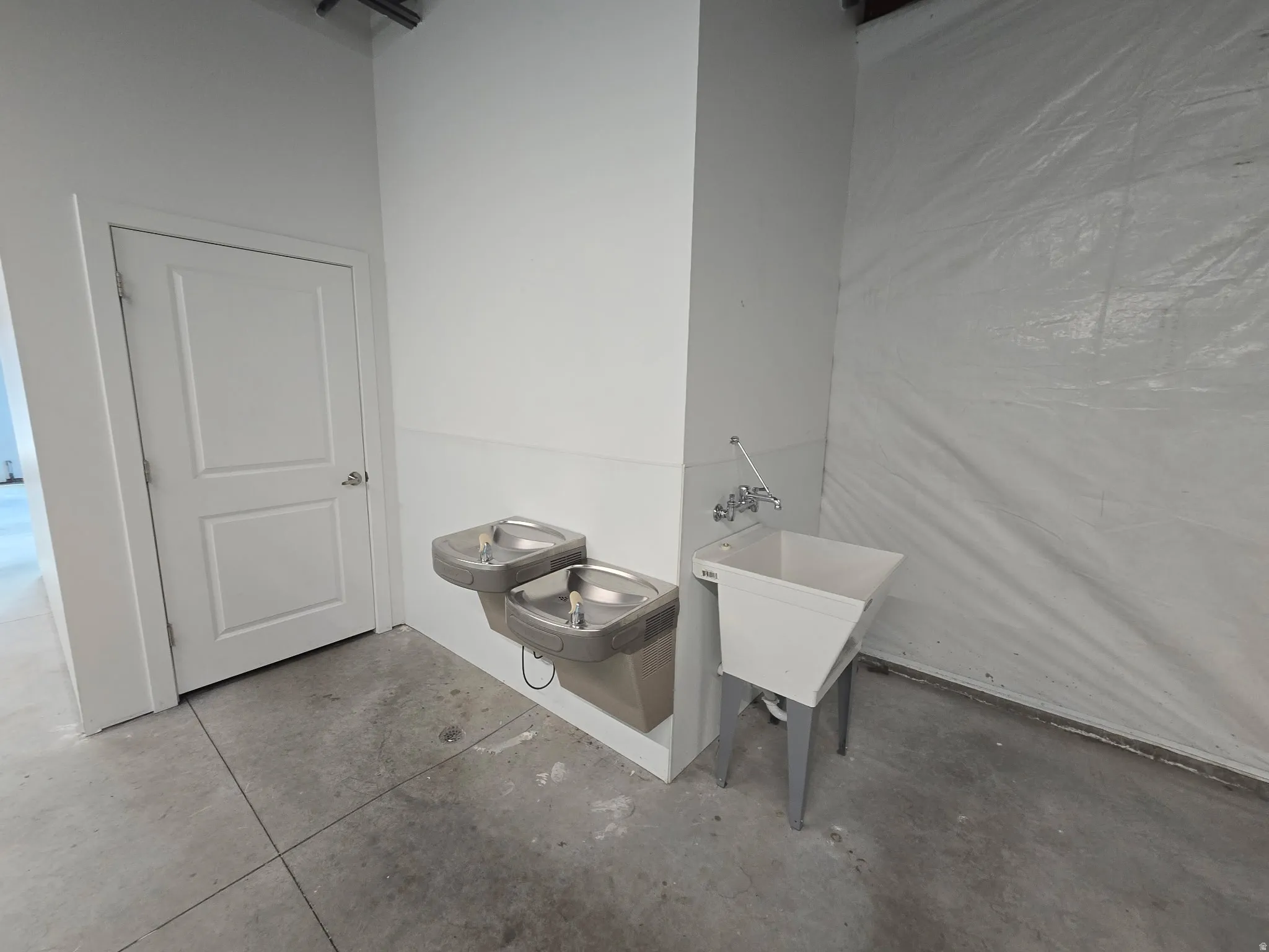 Utility area featuring two built-in stainless steel drinking fountains, a wall-mounted utility sink with metal legs, and a solid white paneled door