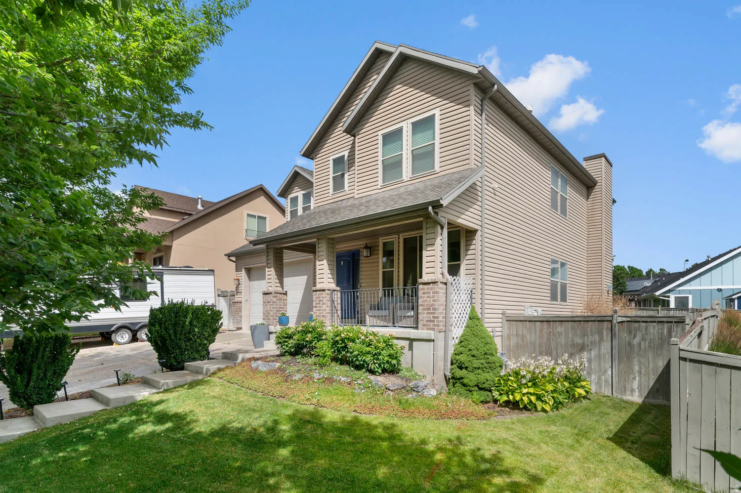 Two-story residence featuring tan horizontal siding, a covered front porch with dark railing, and a gabled roofline