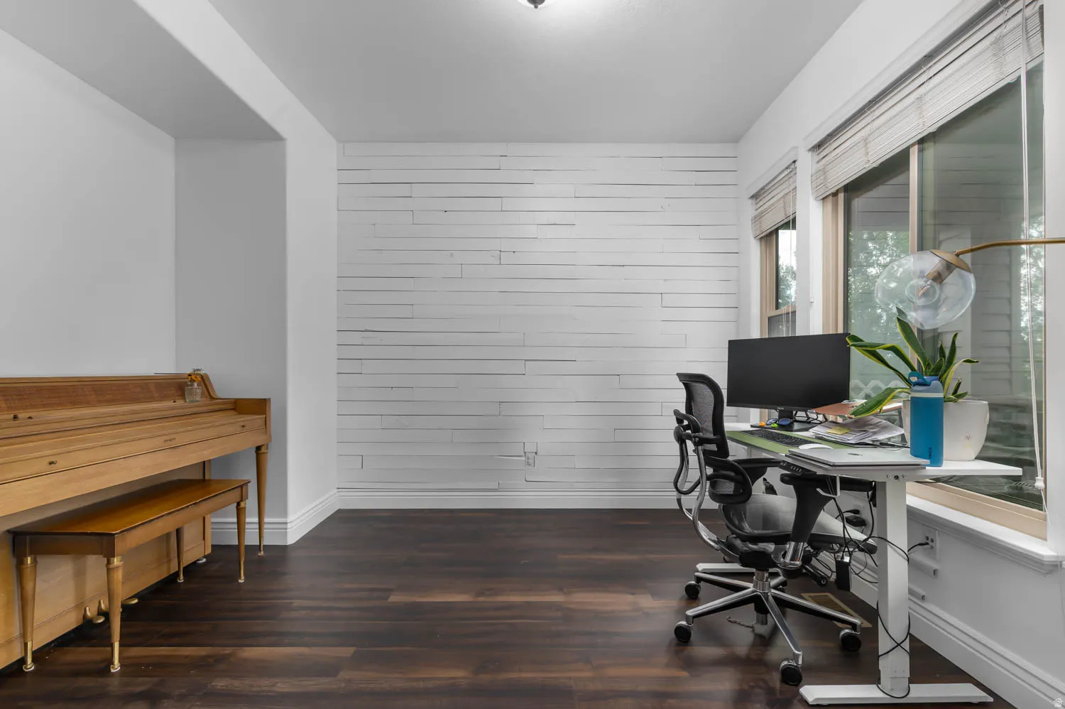 Spacious room featuring dark wood-finish flooring, a white shiplap accent wall, and natural light from large windows