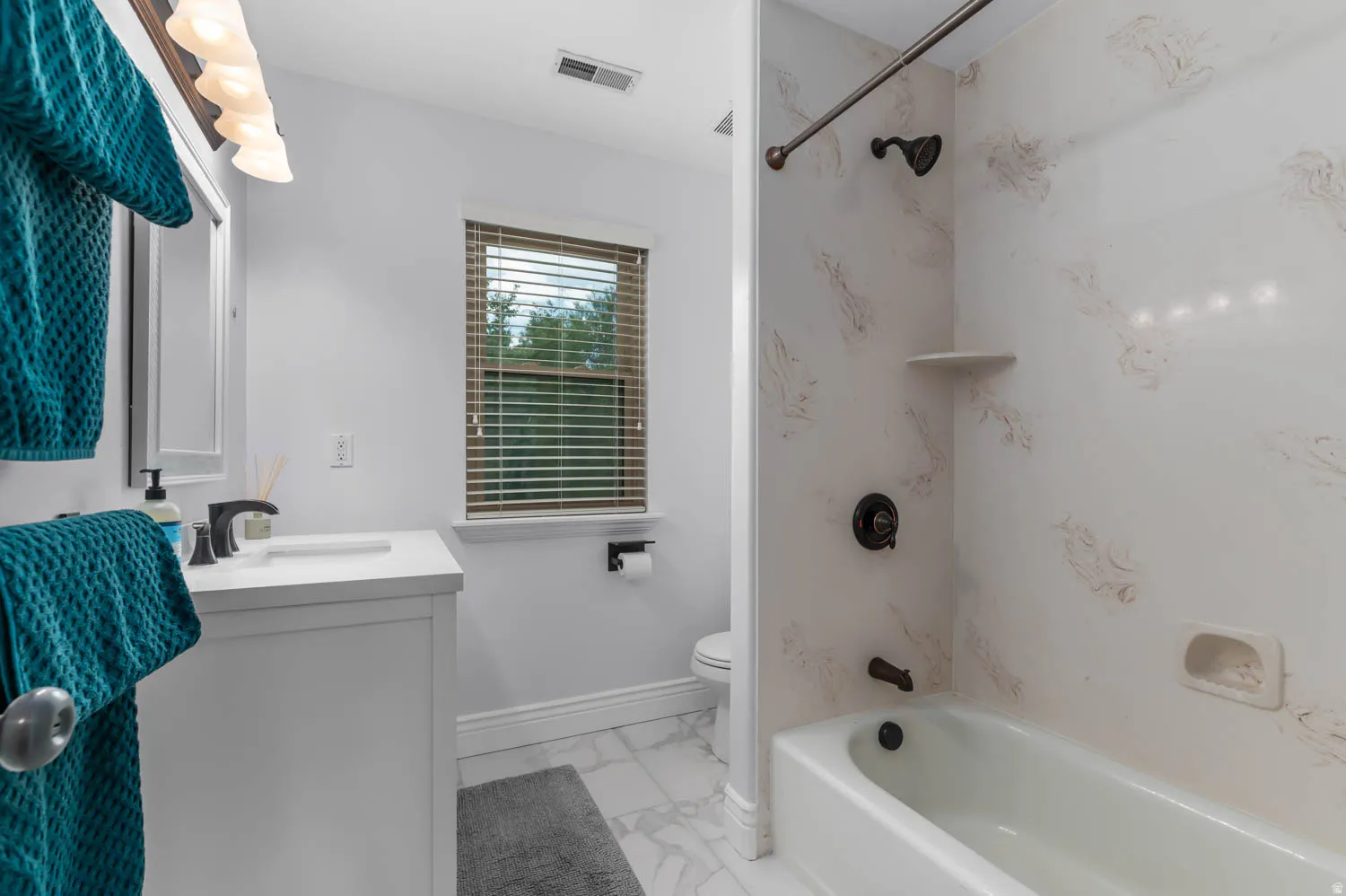 Bathroom featuring a white vanity with integrated sink, dark bronze fixtures, marble-look floor tiling, and a tub/shower combination with patterned wall surround