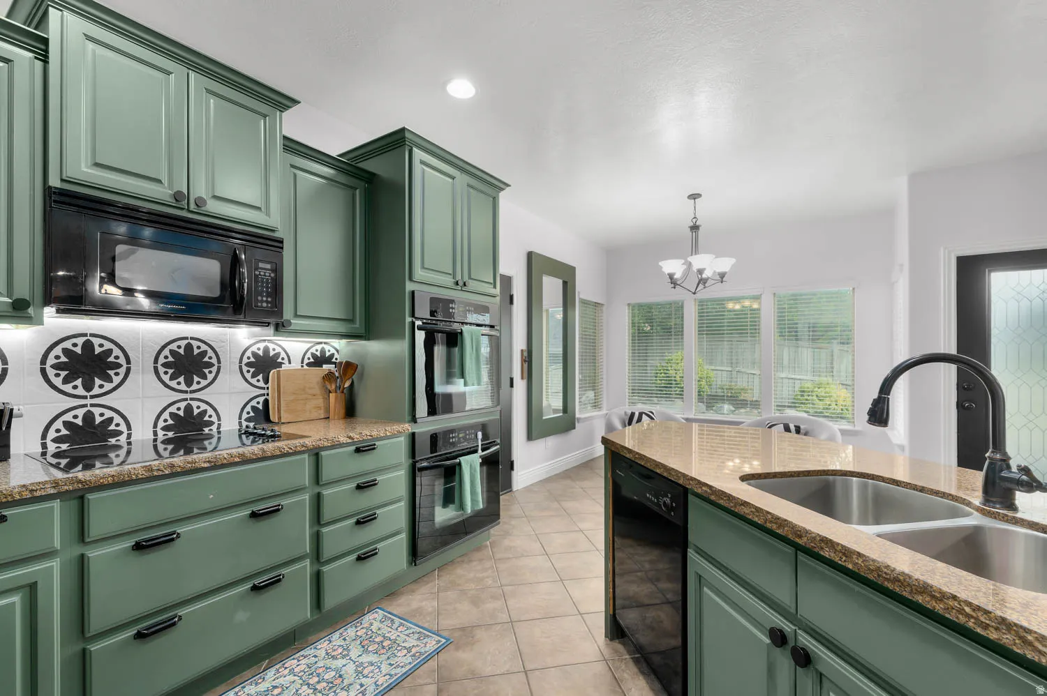 Sage green cabinetry with black hardware, granite countertops, and a striking patterned tile backsplash