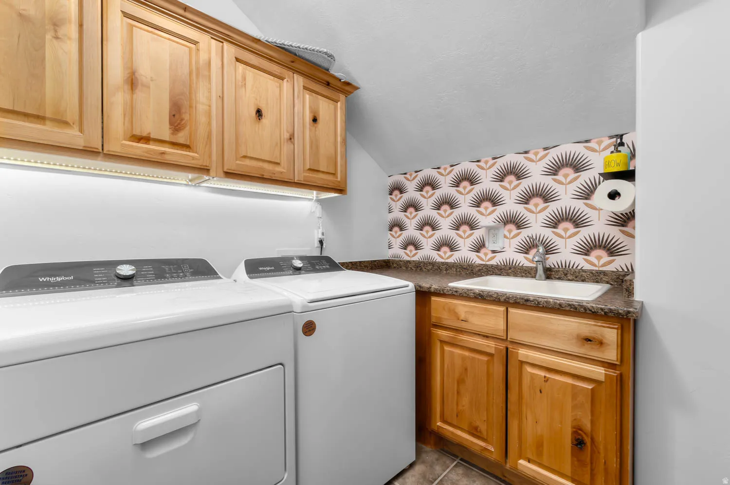 Laundry area featuring wood-finish cabinetry, an integrated sink, and a decorative backsplash