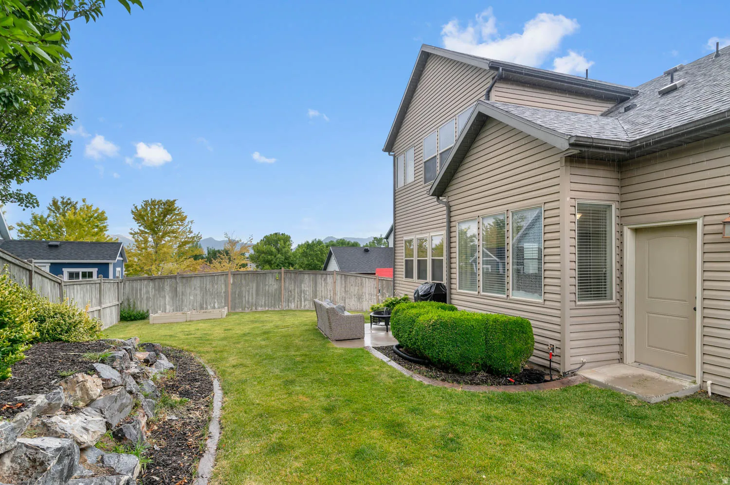 Expansive backyard featuring a manicured lawn, full privacy fencing, and a stone-edged garden bed
