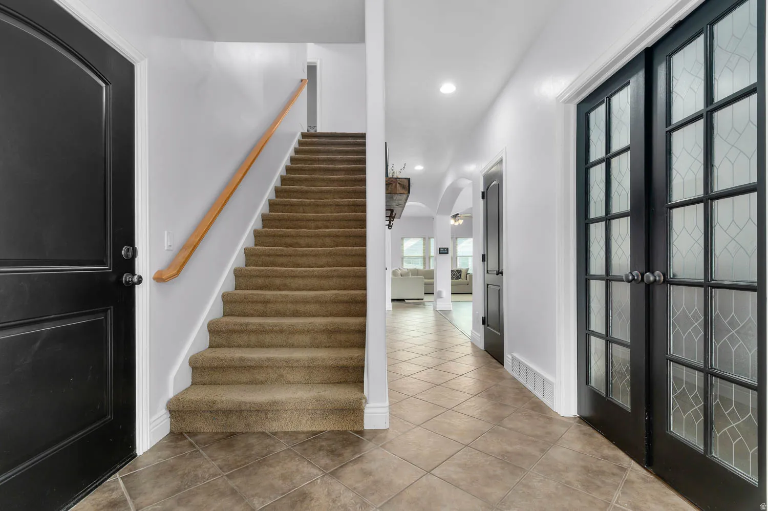Entryway featuring diamond-patterned tile flooring, a carpeted staircase with wood handrail, and black French doors with decorative glass panels