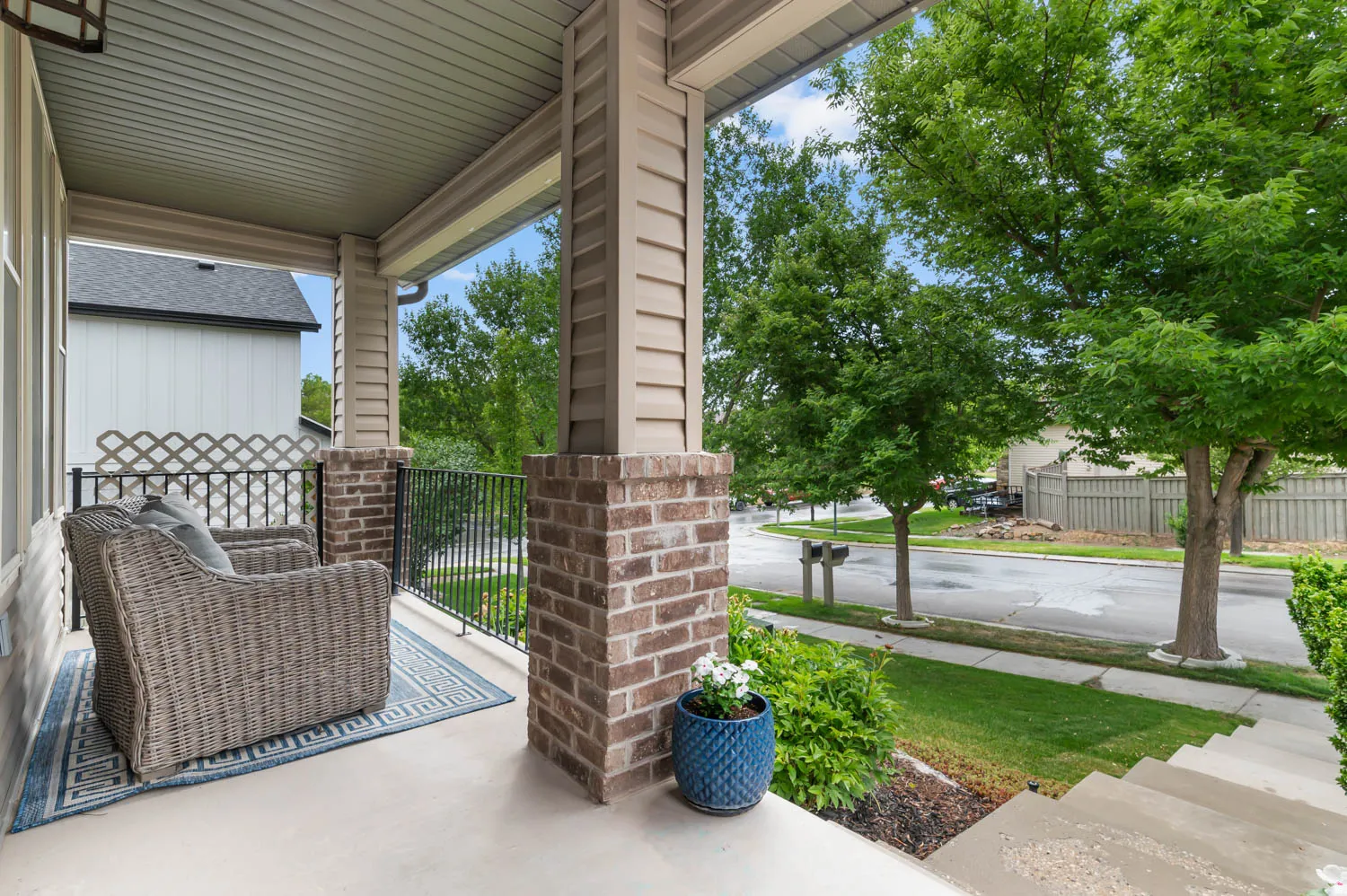 Covered front porch featuring brick and siding pillars, a black metal railing, and concrete flooring
