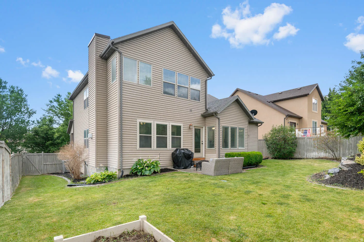 Expansive fenced backyard featuring a patio, mature landscaping, and a substantial two-story exterior with multiple windows