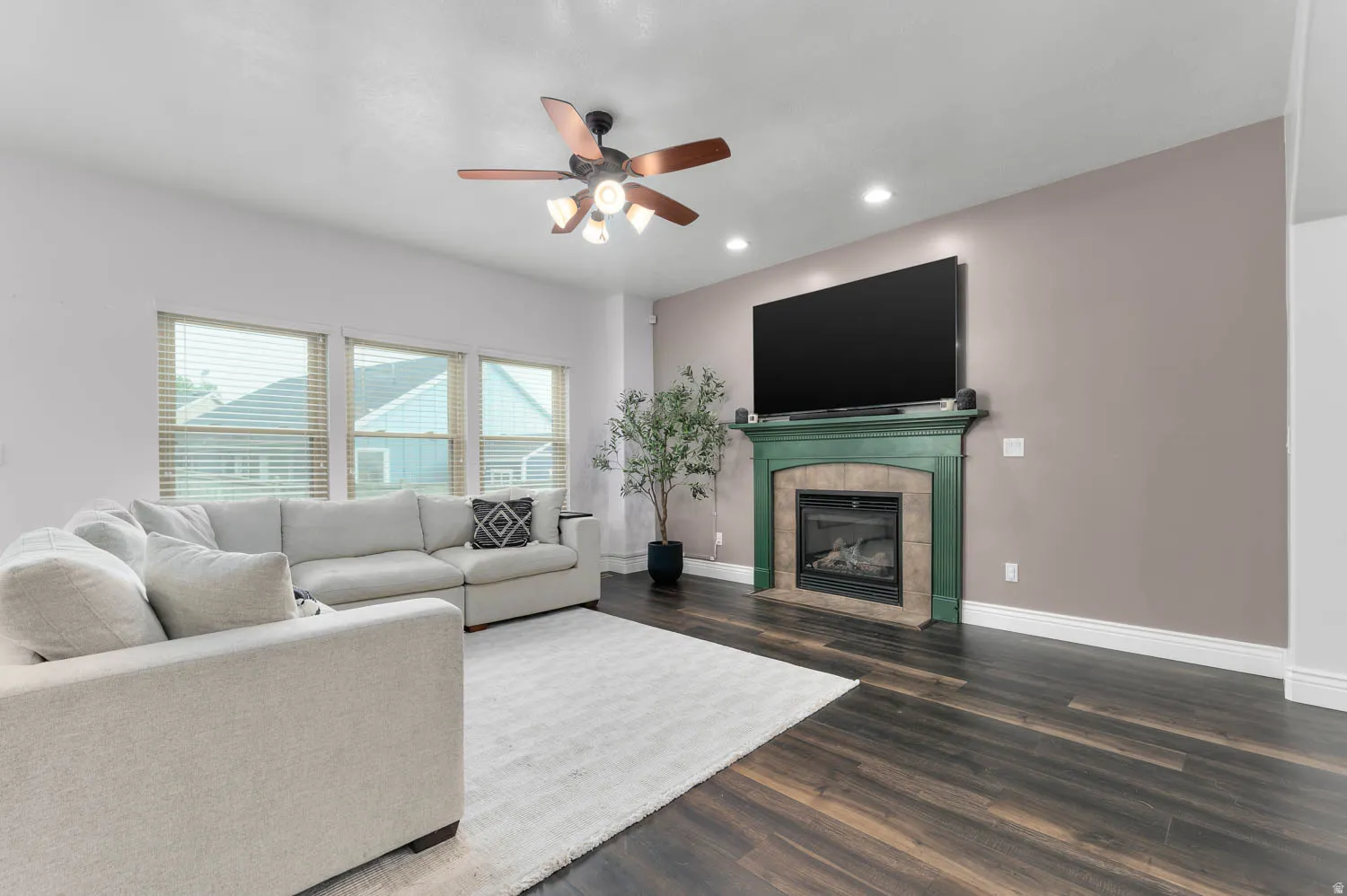 Spacious living area featuring dark wood-finish flooring and a ceiling fan with integrated lighting