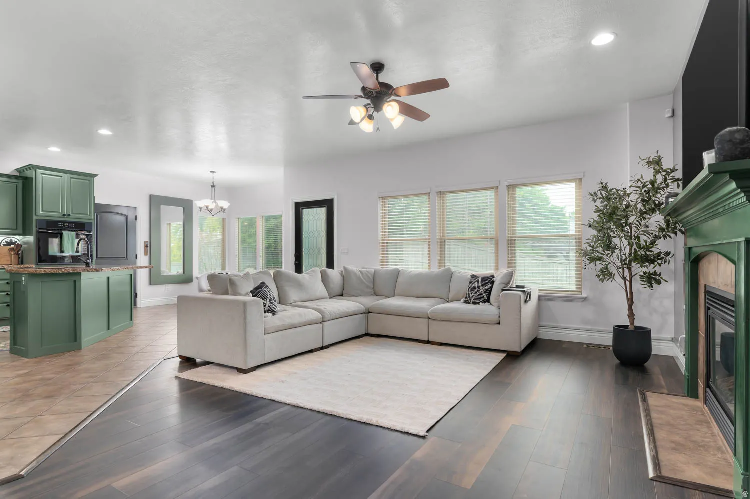 Spacious living area featuring dark wood-finish flooring, a ceiling fan, and multiple windows with blinds