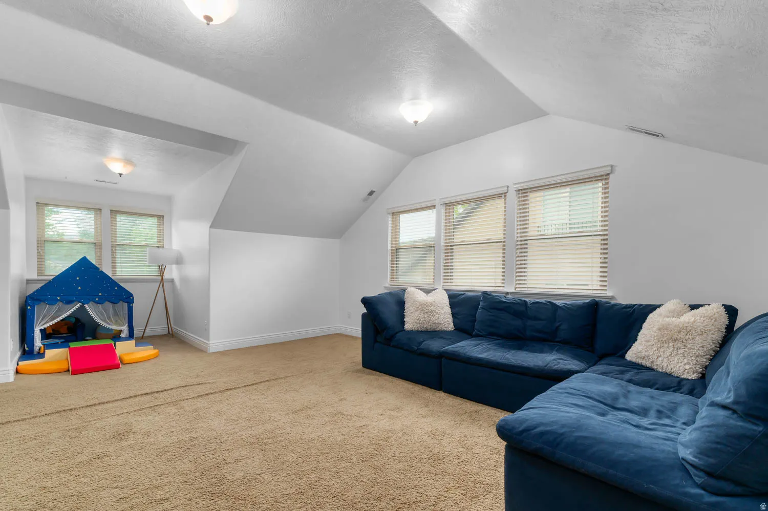 Carpeted room with white walls, multiple windows featuring blinds, and sloped ceiling details