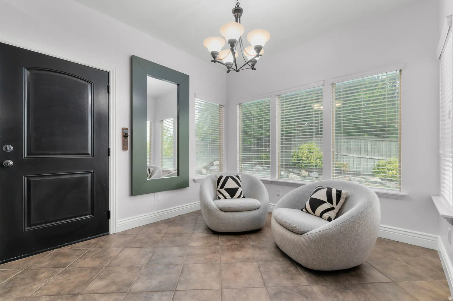 Foyer featuring large format tile flooring, a paneled entry door, a multi-light chandelier, and a wall of windows with blinds