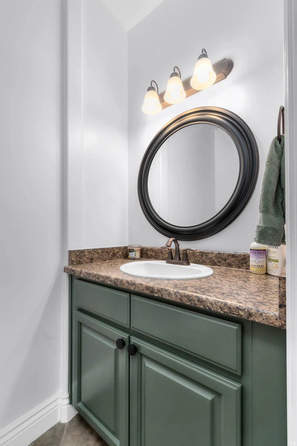 Vanity with green cabinetry, a white oval sink, and a speckled countertop