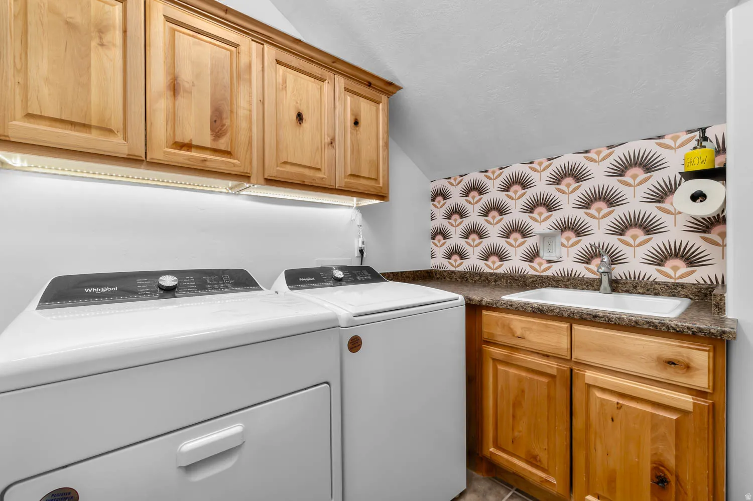 Laundry area featuring wood cabinetry with under-cabinet lighting, a built-in utility sink, and stone-finish countertops