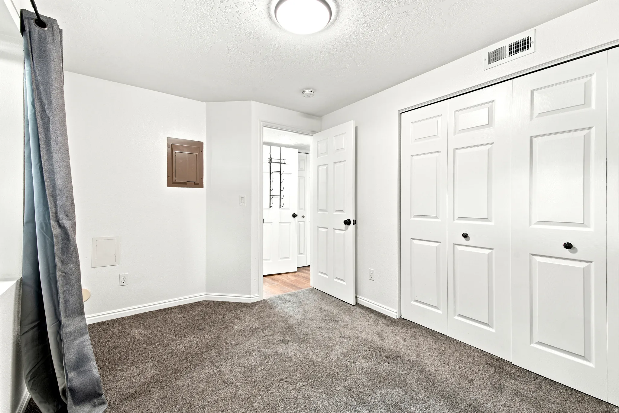 Spacious interior room featuring plush gray carpeting, white walls, and bright overhead lighting