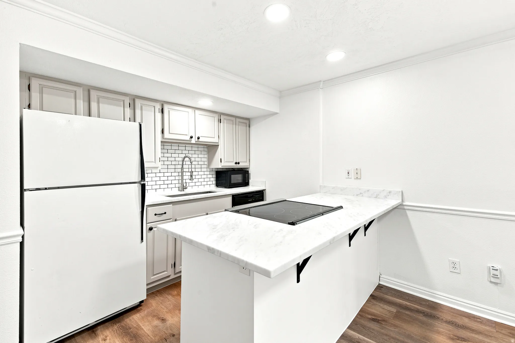 Kitchen featuring a built-in cooktop, light-toned cabinetry, white subway tile backsplash, and a white refrigerator