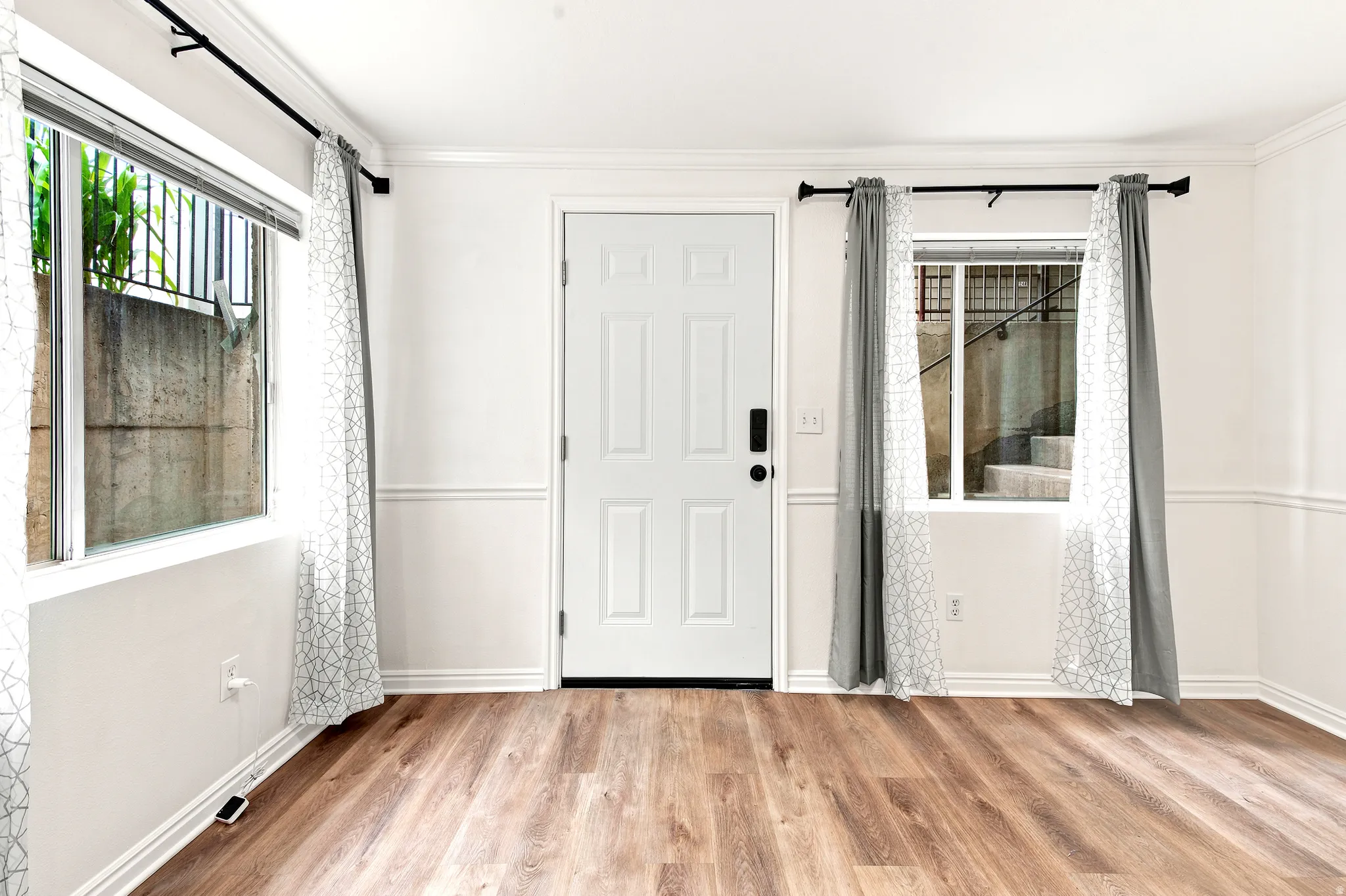 Wood-finish flooring throughout, white paneled door, two large windows, white crown molding, and wainscoting