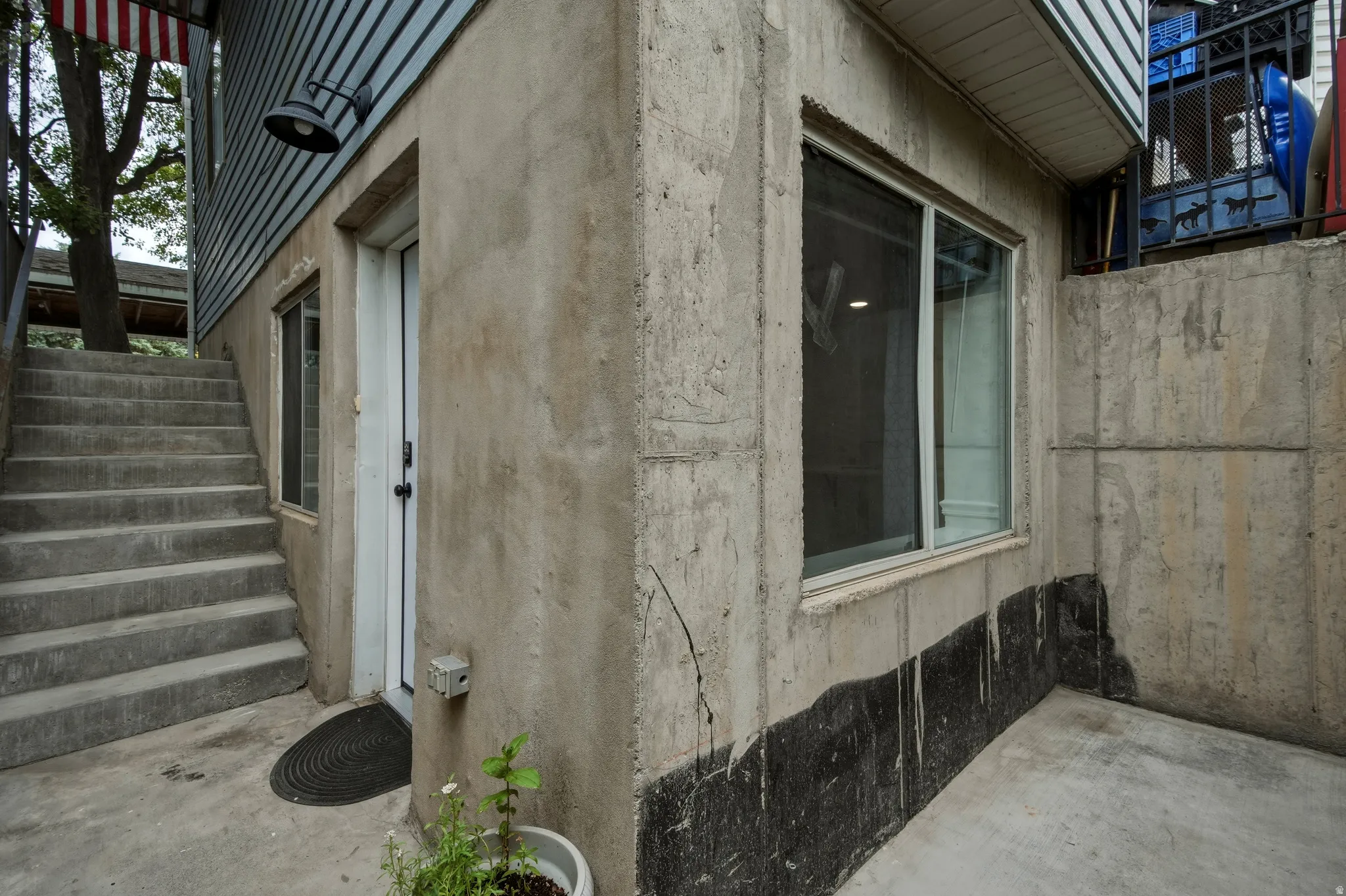 Concrete exterior with a white entry door, recessed window, and exterior wall-mounted light fixture