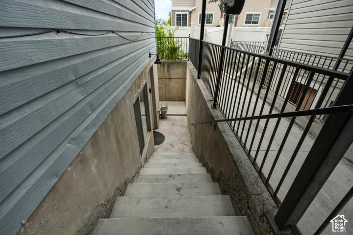 Exterior access staircase featuring concrete steps, a black metal handrail, and a black metal balustrade