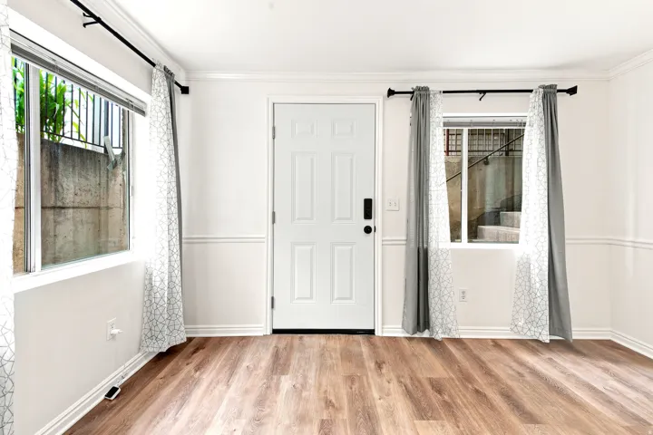 Wood-finish flooring throughout, white paneled door, two large windows, white crown molding, and wainscoting