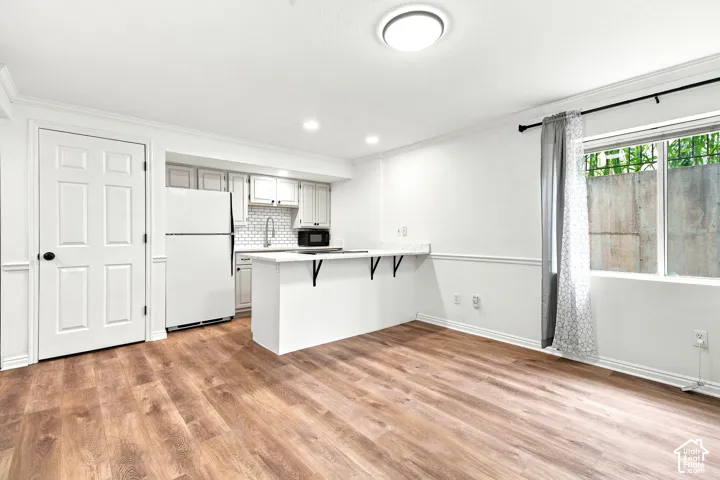 Open-concept living space featuring wood-finish flooring, a contemporary kitchen area, white cabinetry, and a subway tile backsplash