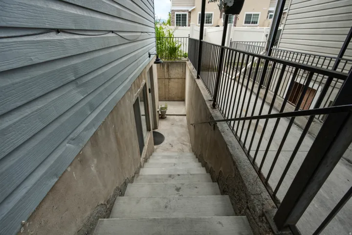 Exterior access staircase featuring concrete steps, a black metal handrail, and a black metal balustrade