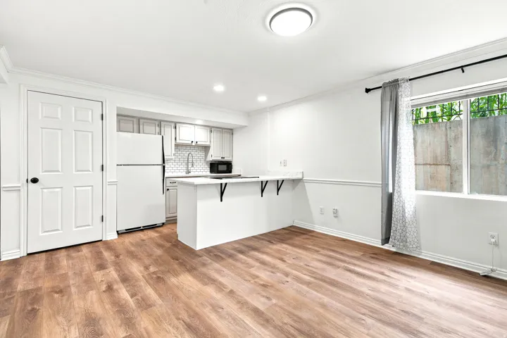 Open-concept living space featuring wood-finish flooring, a contemporary kitchen area, white cabinetry, and a subway tile backsplash