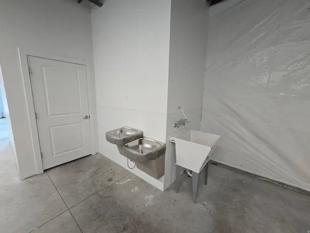 Utility area featuring two built-in stainless steel drinking fountains, a wall-mounted utility sink with metal legs, and a solid white paneled door