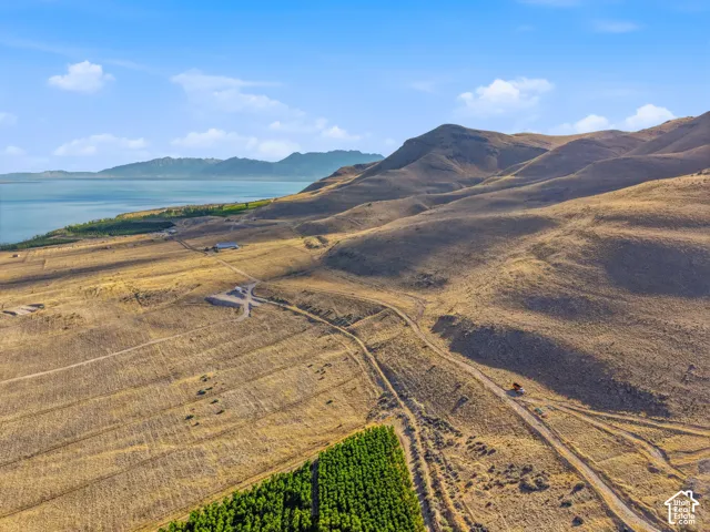 Expansive undeveloped land featuring rolling hills, a large body of water, and distant mountains under a blue sky