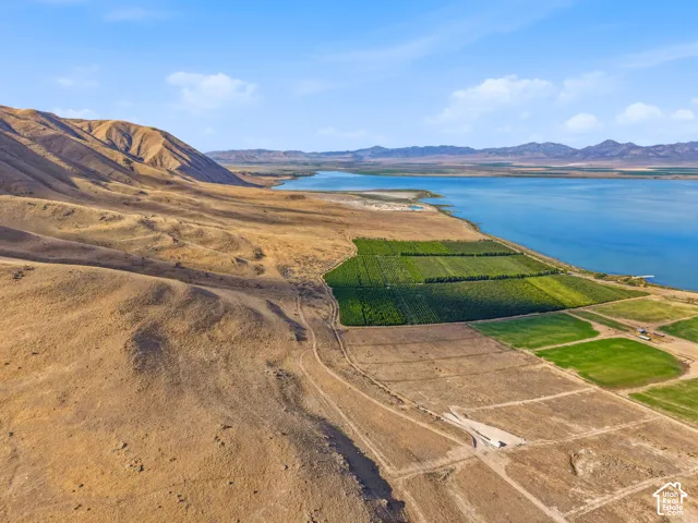 Expansive waterfront property with diverse topography featuring cultivated green fields, natural golden hillsides, a clear blue lake, and distant mountain ranges