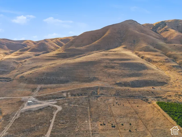 Expansive land parcel featuring rolling hills, a cultivated field, and a small structure