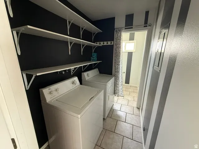 Laundry area featuring white appliances, a black accent wall with three white shelving units, and light-toned tile flooring