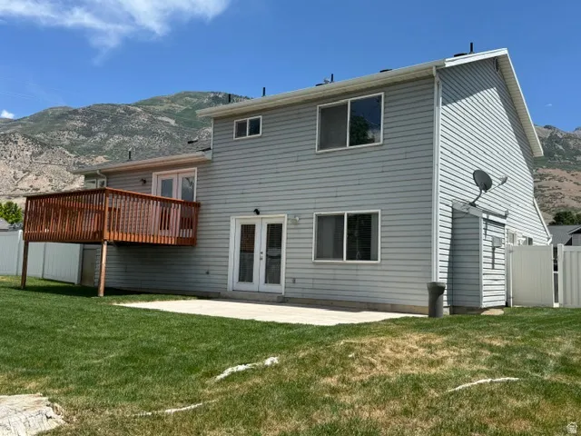 Rear exterior with a wood deck, ground-level patio, and a landscaped lawn