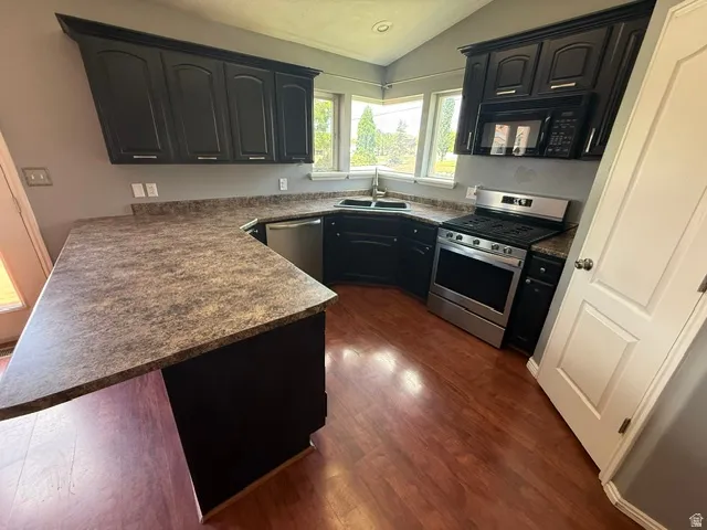 Kitchen featuring dark cabinetry, laminate countertops, wood-finish flooring, stainless steel appliances, and corner windows