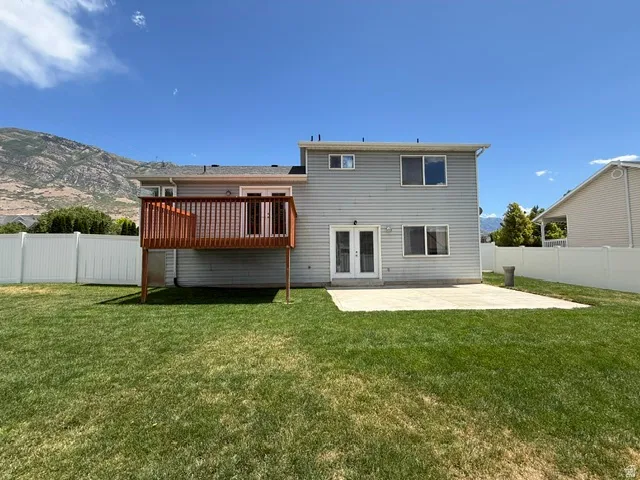 Expansive backyard featuring a wood deck, concrete patio, vinyl privacy fencing, and a mountain backdrop