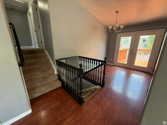 Interior landing featuring rich wood-finish flooring, a contemporary chandelier, and French doors opening to a wood deck