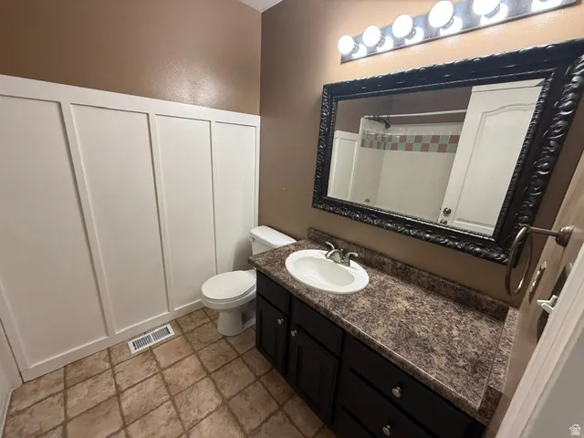Bathroom featuring board and batten wall paneling, a dark wood-finish vanity with a single basin sink, a speckled countertop, and an ornate framed mirror