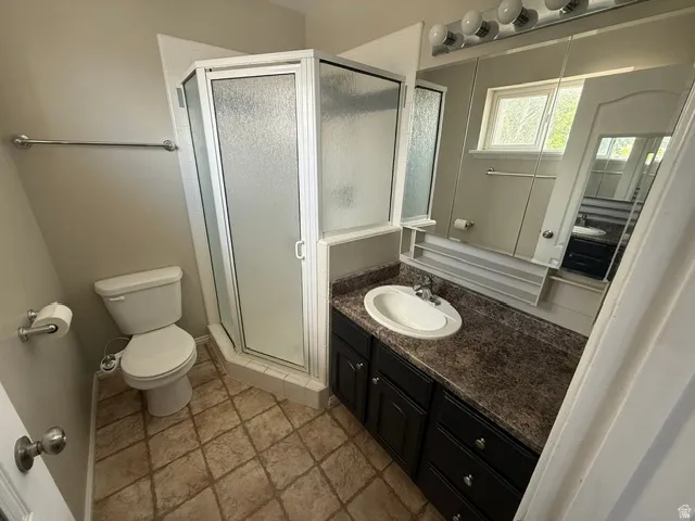Bathroom featuring a shower stall with frosted glass, a dark wood-finish vanity with a speckled countertop, an integrated sink, a large wall-mounted mirror, and tile flooring