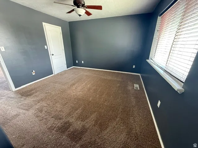 Room featuring plush brown carpeting, a ceiling fan with light fixture, and a window with horizontal blinds