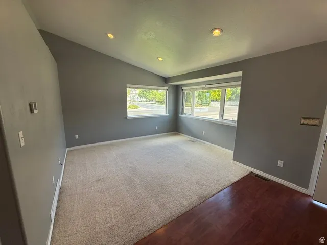 Spacious living area featuring a vaulted ceiling with recessed lighting, large windows, and a combination of carpet and wood-finish flooring
