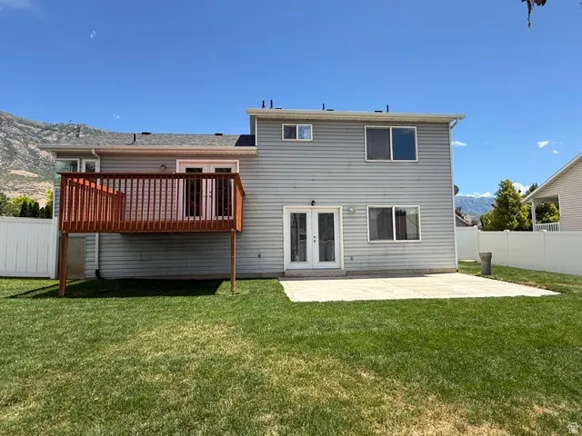Expansive backyard featuring a manicured lawn, a raised wooden deck with railings, a ground-level concrete patio, and a white vinyl fence
