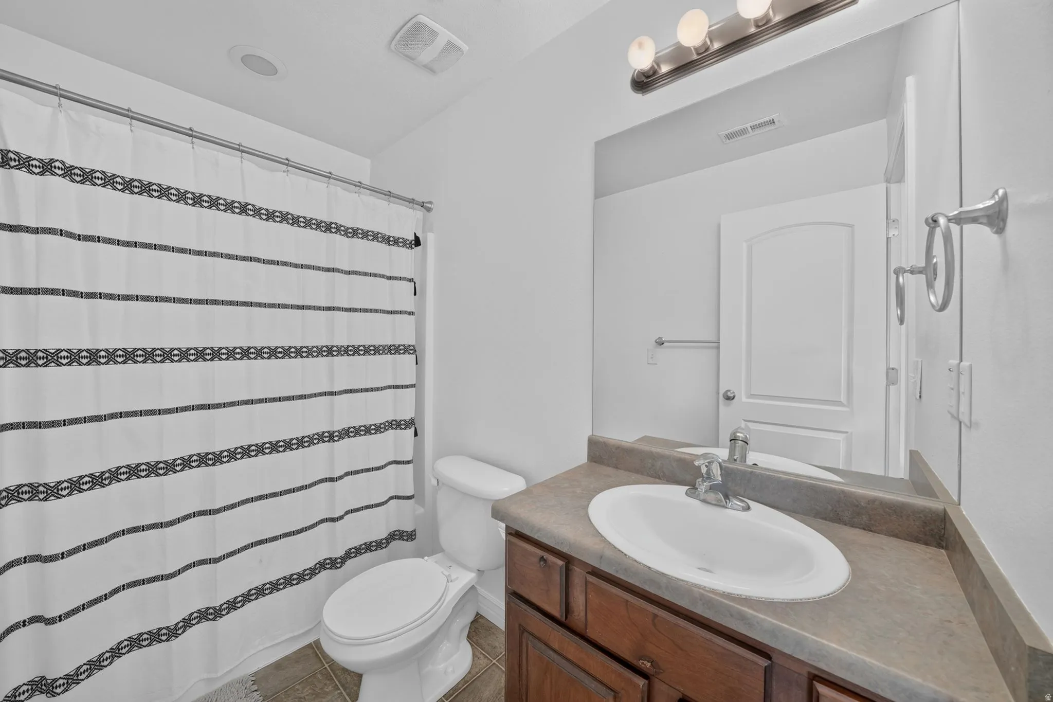 Bathroom featuring a dark wood vanity with an integrated sink, a large wall mirror, and overhead vanity lighting