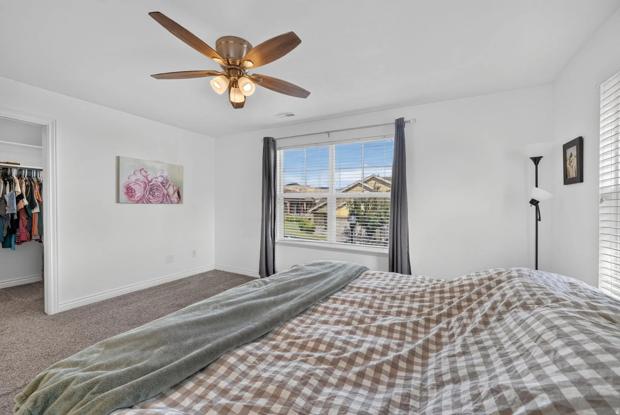 Carpeted bedroom featuring a large window with blinds, a ceiling fan with integrated lighting, and an open closet