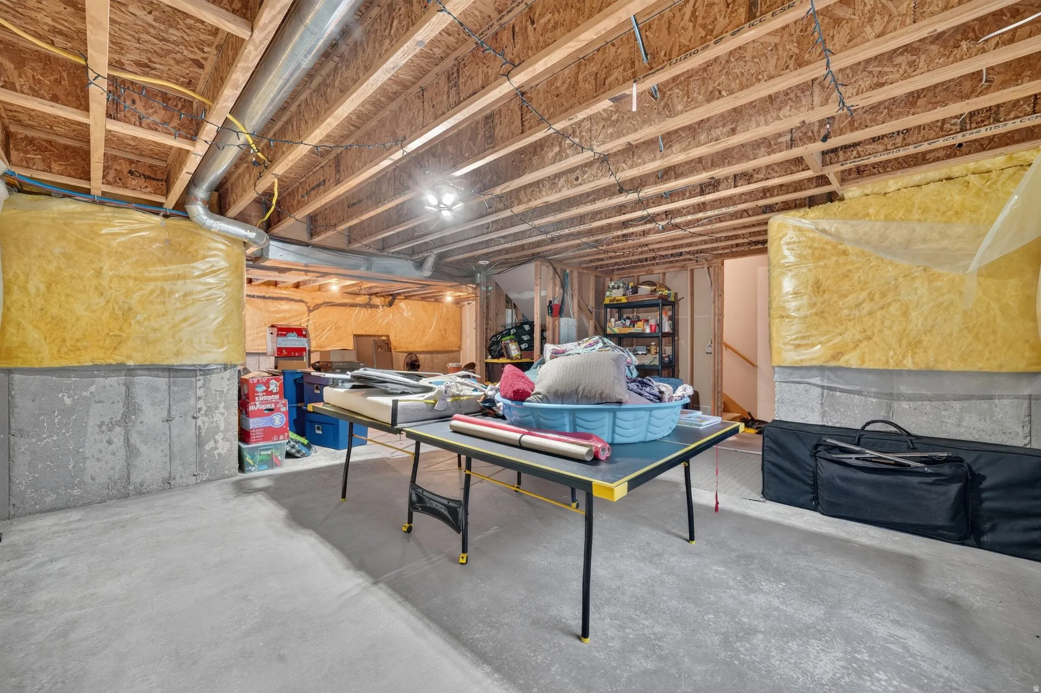 Unfinished basement with concrete flooring, exposed wood joists, and concrete foundation walls