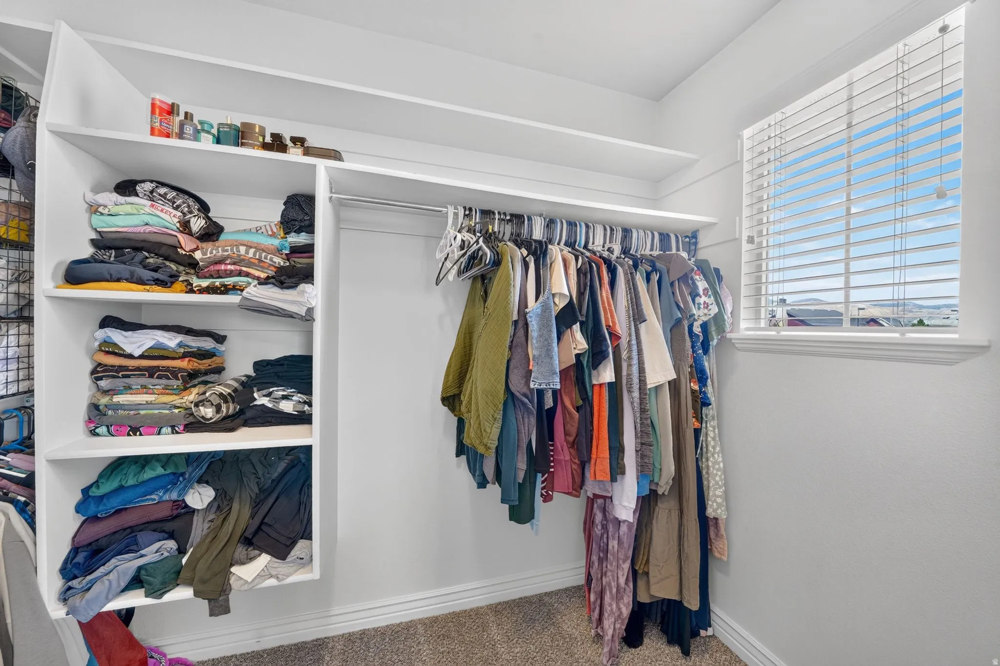 Walk-in closet featuring built-in white shelving, integrated hanging rods, and a window with blinds