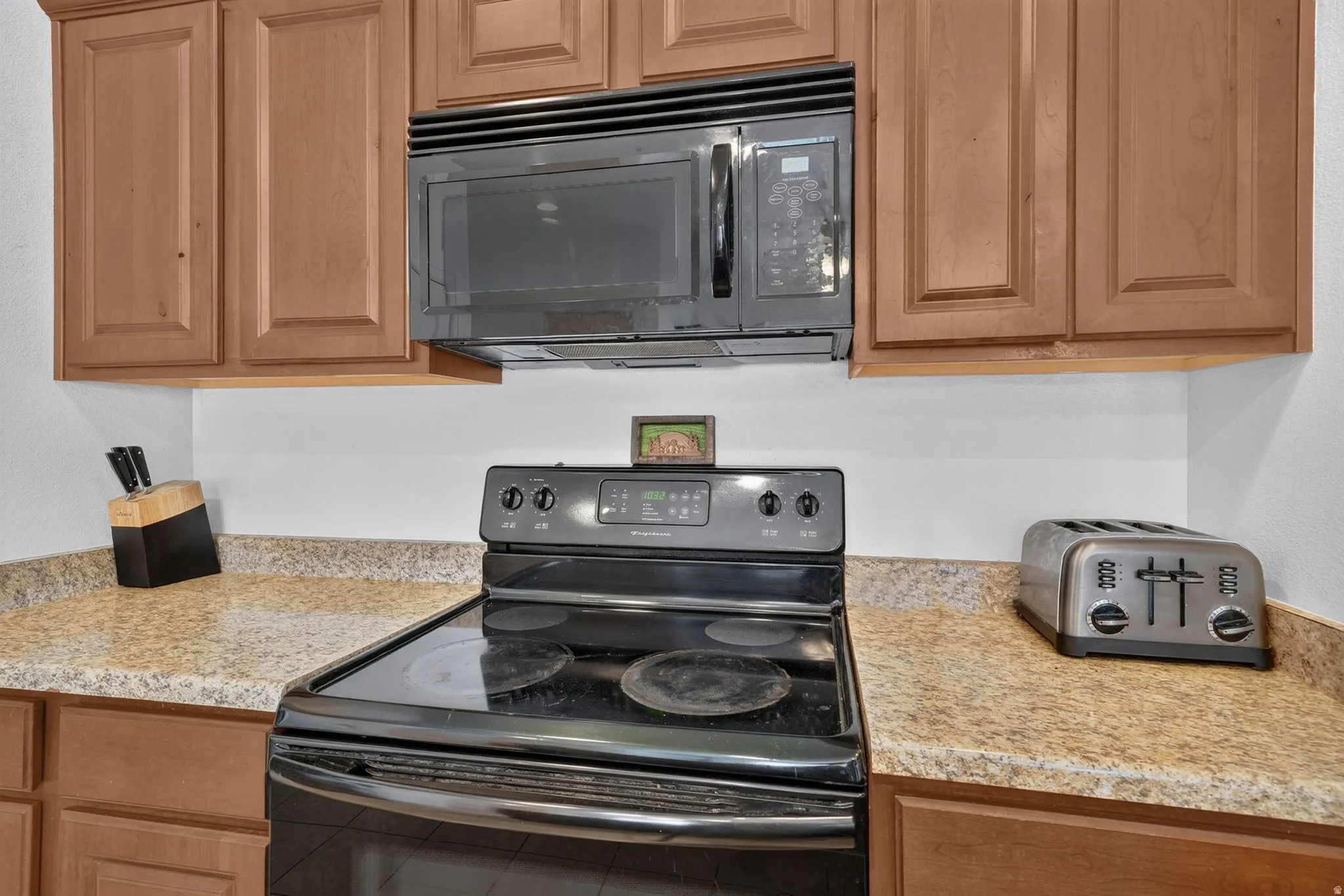 Kitchen featuring wood-finish cabinetry, speckled countertops, a black electric range, and an integrated black microwave above