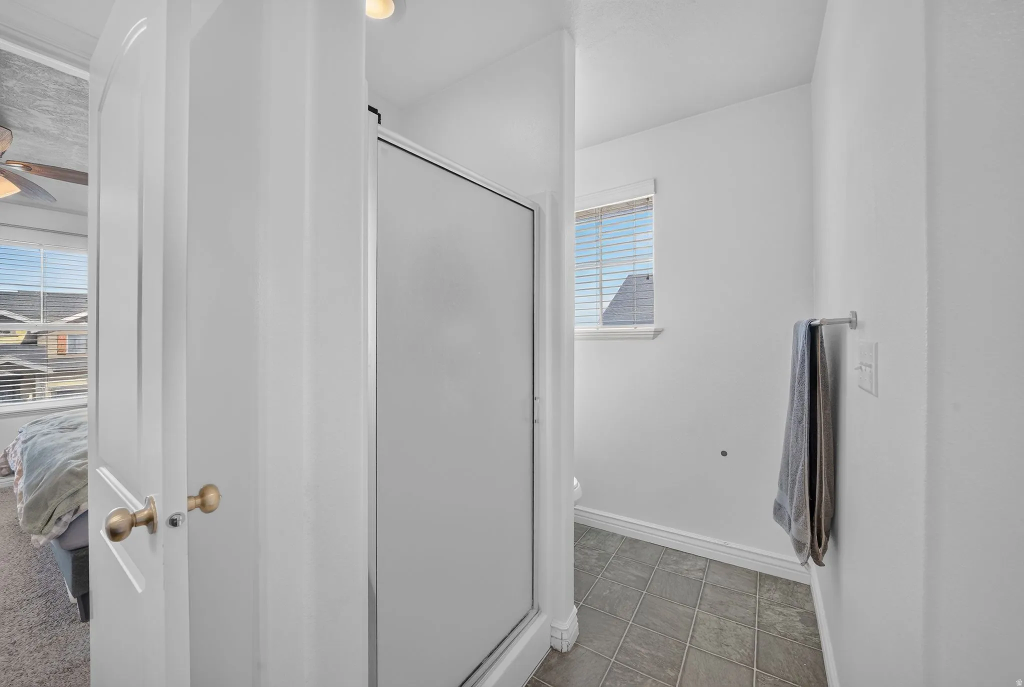 Enclosed shower with frosted glass, complemented by a window with horizontal blinds, and square floor tiling