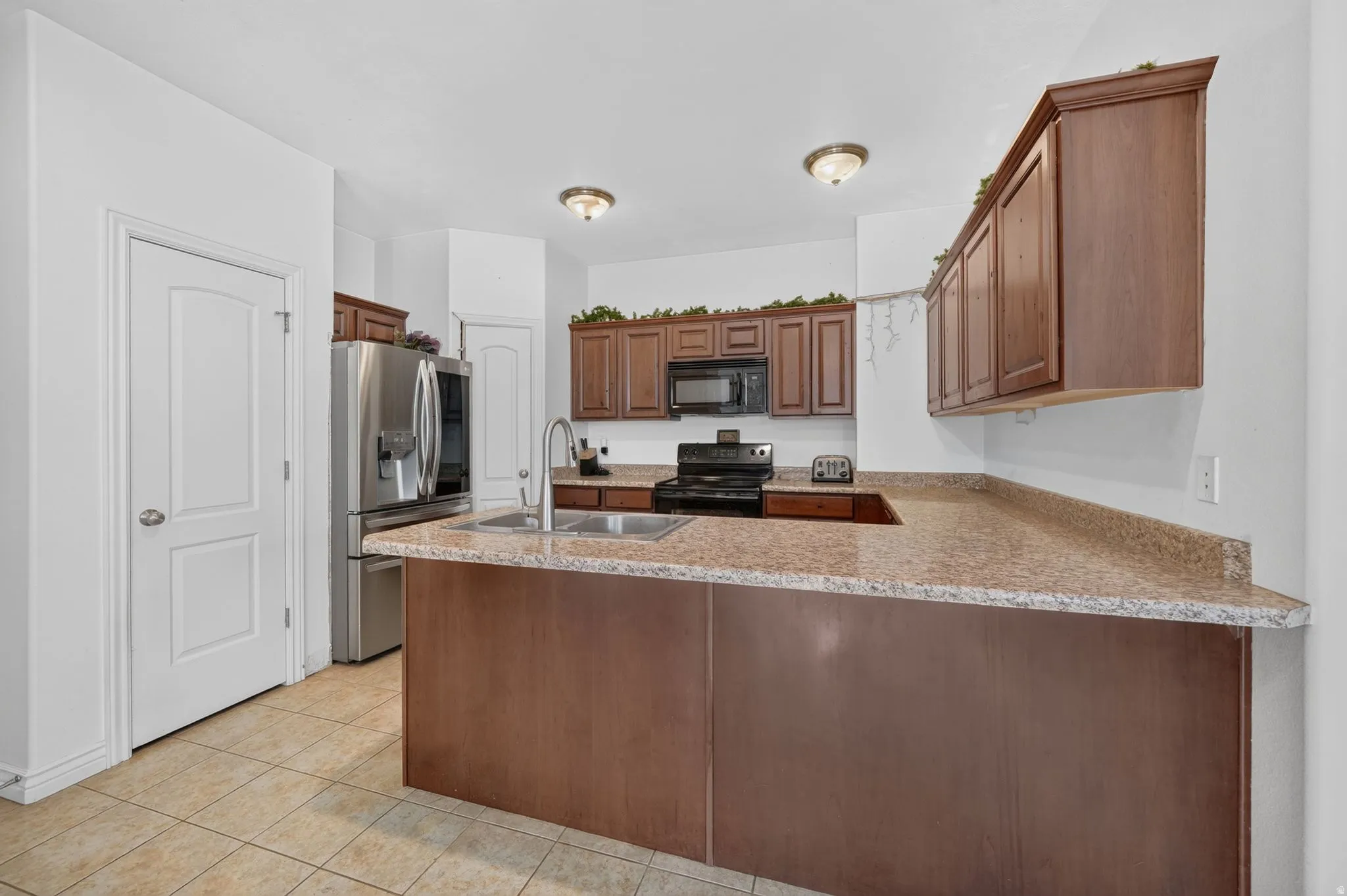 Kitchen featuring wood-finish cabinetry, speckled countertops, stainless steel refrigerator, black range, and dual-basin sink