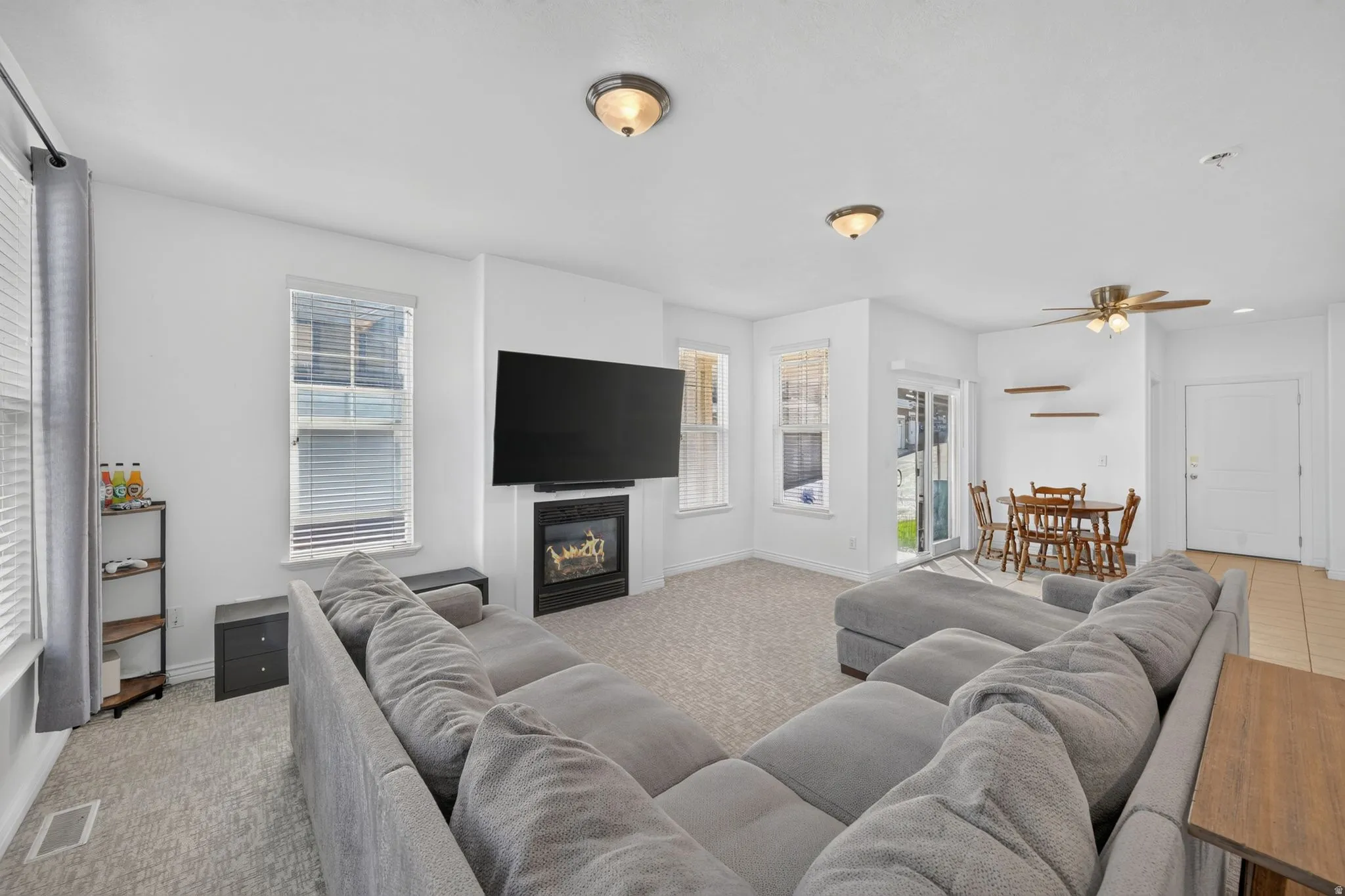 Open-concept living space featuring a built-in fireplace, multiple windows with blinds, a ceiling fan with light fixture, and tile flooring